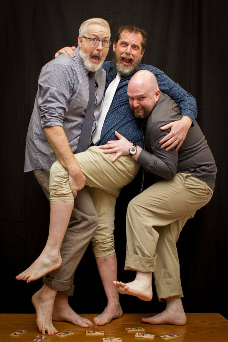 Three men hugging each other and standing barefoot over a floor covered with live mousetraps